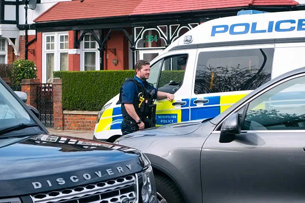 Beckenham, Kent, England April 1, 2016: A Metropolitan Police officer standing beside a van at a nearby incident in a suburban street in Greater London. Several other officers were in the vicinity, many of them armed, and a number of unmarked police vehicles formed a road block